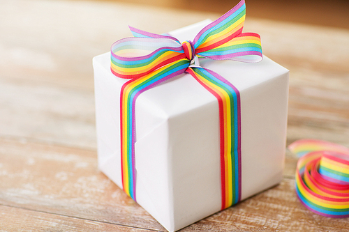 homosexual and lgbt concept - close up of gift box with gay pride awareness ribbon on wooden table at home