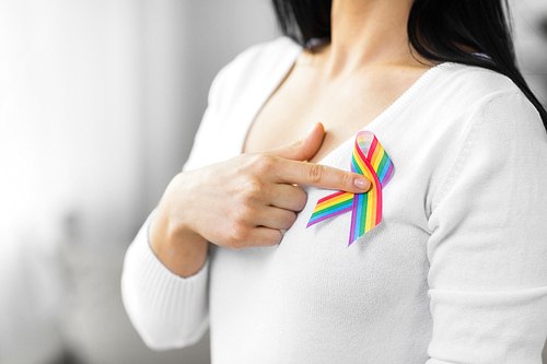 homosexual and lgbt concept - close up of woman showing gay pride awareness ribbon on her chest