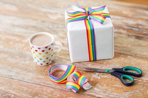 homosexual and lgbt concept - cup of coffee or cacao drink with gift box, gay pride awareness ribbon and scissors on wooden table