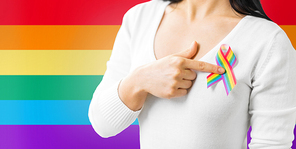 homosexual and lgbt concept - close up of woman showing gay pride awareness ribbon on her chest over rainbow background