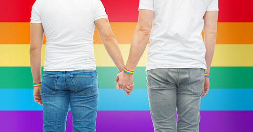 lgbt, same-sex relationships and homosexual concept - close up of male couple wearing gay pride rainbow awareness wristbands holding hands