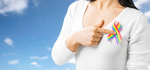 homosexual and lgbt concept - close up of woman showing gay pride awareness ribbon on her chest over blue sky background