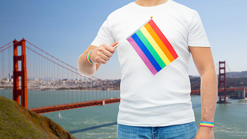 lgbt, same-sex relationships and homosexual concept - close up of man wearing gay pride awareness wristbands holding  flag over golden gate bridge in san francisco bay background