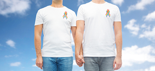 lgbt, same-sex relationships and homosexual concept - close up of male couple with gay pride rainbow awareness ribbons over blue sky and clouds background