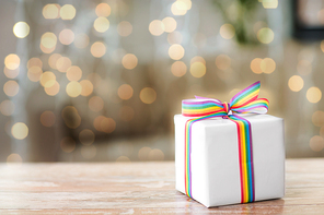 homosexual and lgbt concept - gift box with gay pride awareness ribbon on wooden table over festive lights background