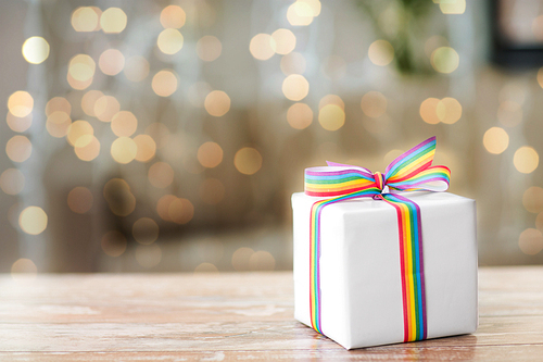homosexual and lgbt concept - gift box with gay pride awareness ribbon on wooden table over festive lights background