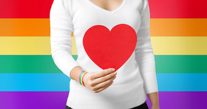 homosexual and lgbt concept - woman holding red heart shape and wearing gay pride awareness ribbon wristband over rainbow background
