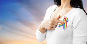 homosexual and lgbt concept - close up of woman showing gay pride awareness ribbon on her chest over evening sky background