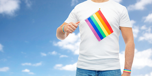 lgbt, same-sex relationships and homosexual concept - close up of man wearing gay pride awareness wristbands holding  flag over blue sky and clouds background