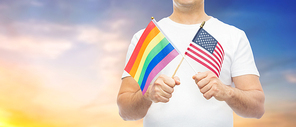 lgbt, same-sex relationships and homosexual concept - close up of man holding gay pride rainbow and american flag over evening sky background