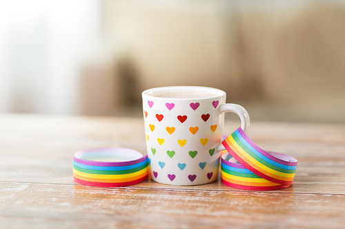 homosexual and lgbt concept - cup with rainbow colored heart pattern and gay pride awareness ribbon on wooden table