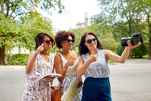 tourism, travel and technology concept - happy women with city guide and map recording video blog by camera in summer park and showing thumbs up