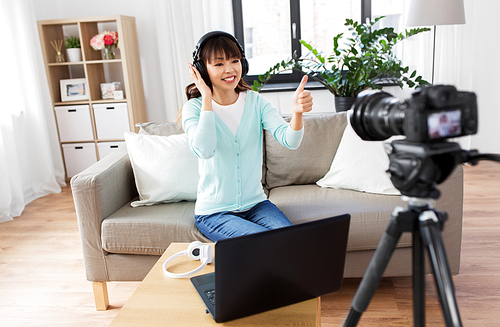 blogging, videoblog and people concept - asian female . with camera and laptop computer recording video review of headphones and showing thumbs up gesture at home