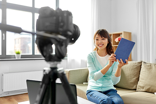 blogging, technology, videoblog and people concept - happy smiling asian woman or . with camera recording video blog of book review at home