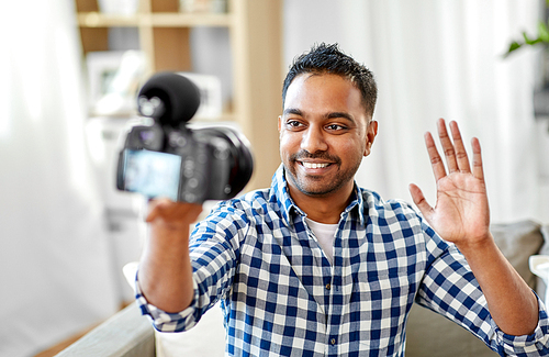 blogging, videoblog and people concept - smiling indian male video . with camera videoblogging and waving hand at home
