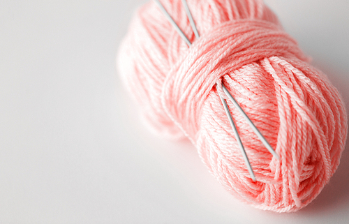 handicraft and needlework concept - knitting needles and ball of yarn in trendy color of the year 2019 living coral