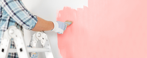 repair and home renovation concept - close up of male hand in gloves painting wall in trendy color of the year2019 living coral