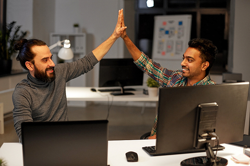 deadline, teamwork and success concept - creative team with computers making high five at night office