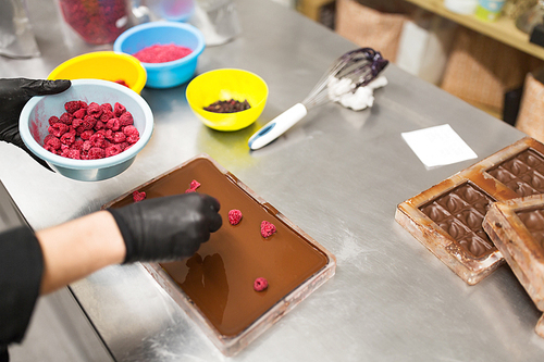 production, cooking and people concept - confectioner making chocolate with raspberries at confectionery shop kitchen