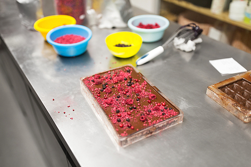 production, cooking and people concept - milk chocolate with berries at confectionery shop kitchen