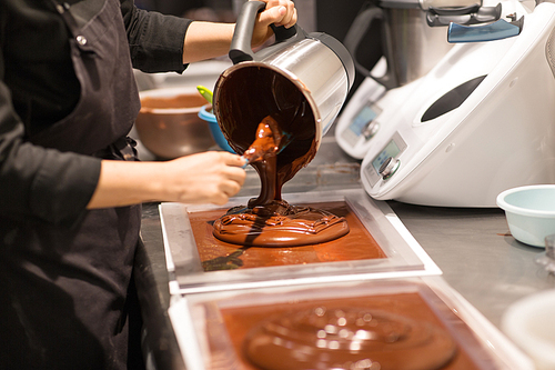 production, cooking and people concept - confectioner filling mold with chocolate at confectionery shop