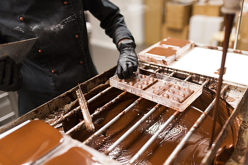 production, cooking and people concept - confectioner removing excess chocolate from mold at confectionery shop