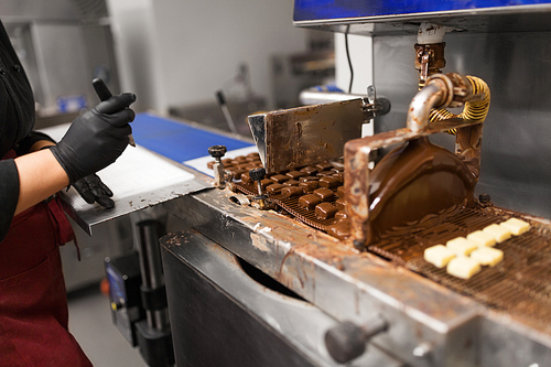 production, candy shop and people concept - confectioner making candies by chocolate coating machine at confectionery