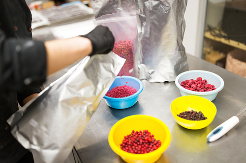 production, cooking and people concept - cook pouring berries into bowl at confectionery shop kitchen