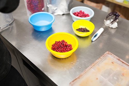 production, cooking and people concept - berries in bowls and whisk at confectionery shop kitchen