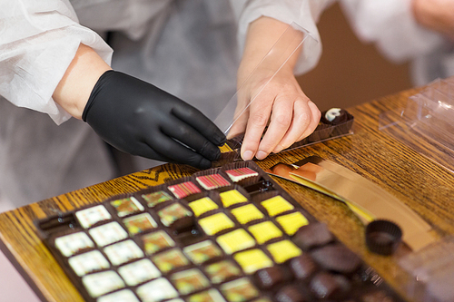 sweets production and industry concept - confectioner or worker packing candies at confectionery shop