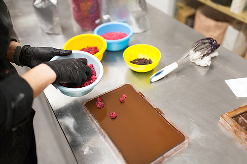 production, cooking and people concept - confectioner making chocolate with raspberries at confectionery shop kitchen