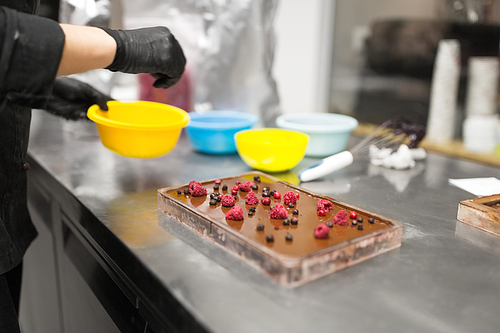 production, cooking and people concept - confectioner making chocolate with berries at confectionery shop kitchen