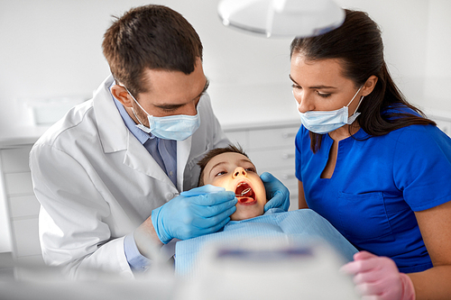 medicine, dentistry and healthcare concept - dentist with mouth mirror checking for kid patient teeth at dental clinic