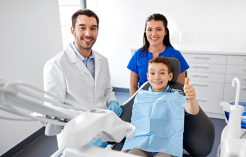 medicine, dentistry and healthcare concept - happy dentist, assistant and kid patient showing thumbs up at dental clinic