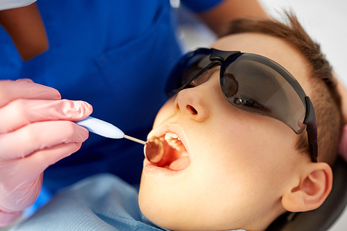 medicine, dentistry and healthcare concept - close up of boy in goggles having teeth checkup with mouth mirror at dental clinic
