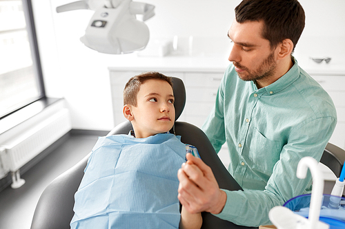 medicine, dentistry and healthcare concept - father supporting son at dental clinic