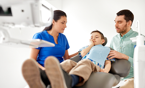 medicine, dentistry and healthcare concept - father and son suffering from toothache visiting dentist at dental clinic