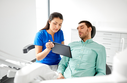 medicine, dentistry and healthcare concept - female dentist with tablet pc computer and male patient discussing teeth treatment at dental clinic office