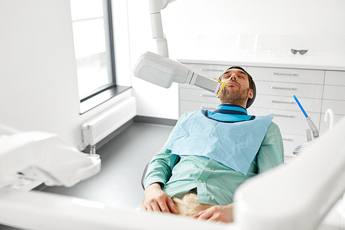 medicine, dentistry and healthcare concept - male patient having x-ray scanning procedure at dental clinic
