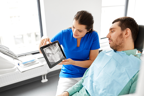 medicine, dentistry and healthcare concept - female dentist showing teeth panoramic x-ray scan on tablet pc computer to male patient at dental clinic