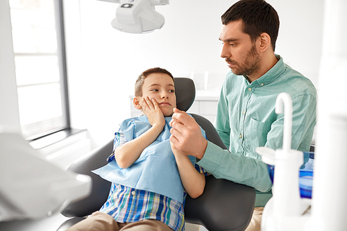 medicine, dentistry and healthcare concept - father supporting son suffering from toothache at dental clinic