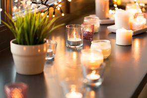 hygge, decoration and christmas concept - candles burning in lanterns and festive garland on window sill at home