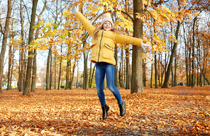 childhood, season and people concept - happy girl jumping at autumn park