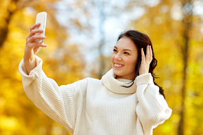 season, technology and people concept - beautiful young happy woman taking selfie by smartphone at autumn park