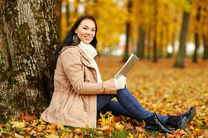 season, technology and people concept - young woman reading book at autumn park