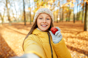 season and people concept - happy girl with apple taking selfie at autumn park