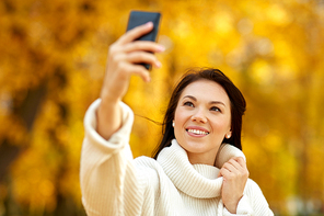 season, technology and people concept - beautiful young happy woman taking selfie by smartphone at autumn park