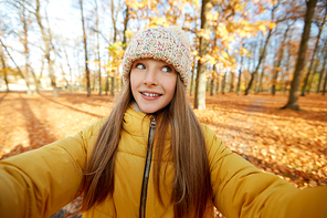 season and people concept - happy girl taking selfie at autumn park