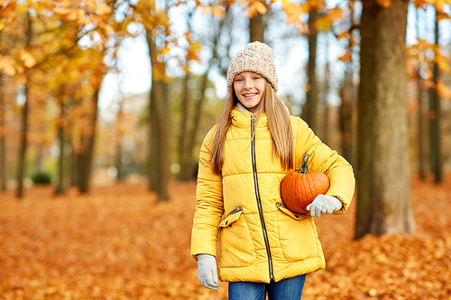 childhood, season and people concept - happy girl with pumpkin at autumn park