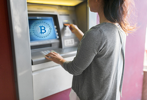 finance, cryptocurrency and technology concept - close up of woman hand inserting bank card to atm machine with bitcoin icon on screen